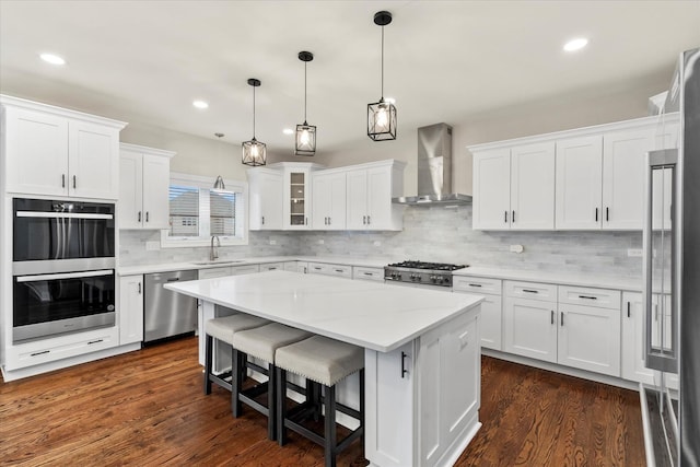 kitchen featuring a kitchen island, white cabinetry, sink, stainless steel appliances, and wall chimney range hood