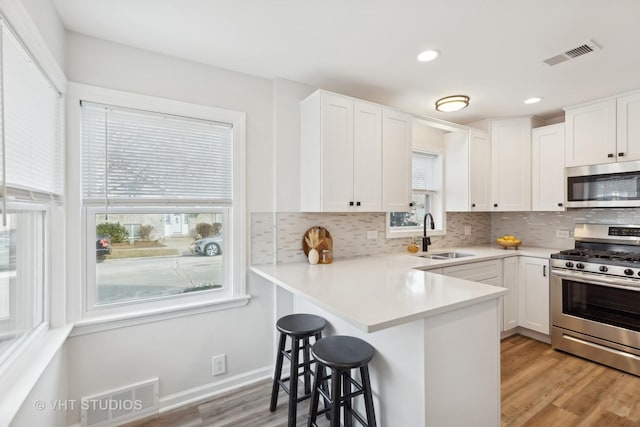 kitchen with sink, white cabinets, a kitchen breakfast bar, kitchen peninsula, and stainless steel appliances