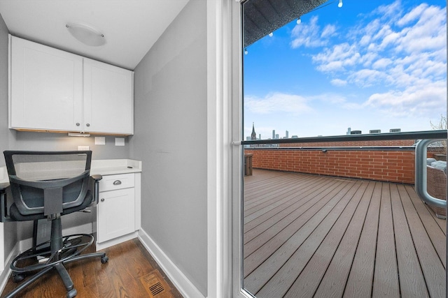 office with dark wood-type flooring, lofted ceiling, brick wall, and built in desk