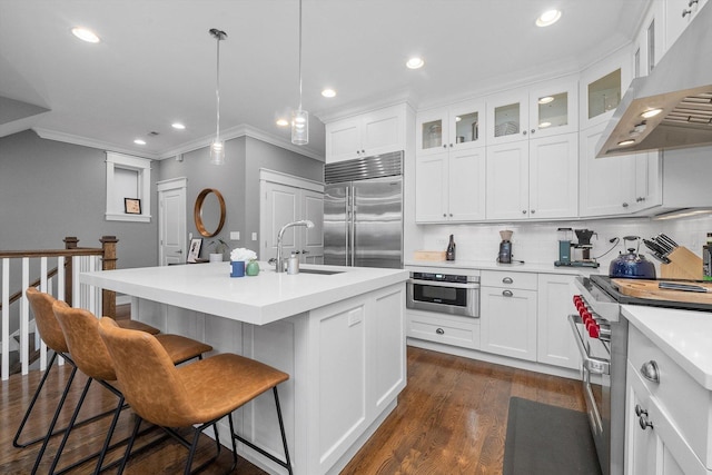 kitchen featuring wall chimney range hood, sink, high quality appliances, white cabinets, and a center island with sink