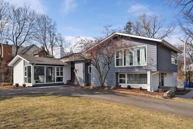 view of front of house featuring a sunroom, a chimney, aphalt driveway, and a front yard