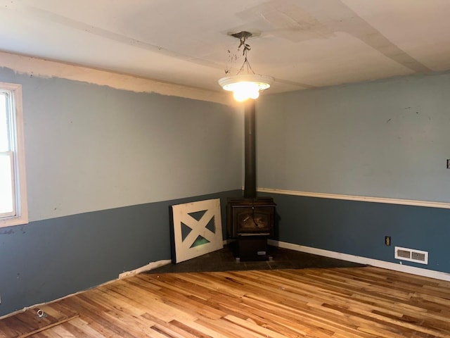 unfurnished living room featuring wood-type flooring, a wealth of natural light, and a wood stove