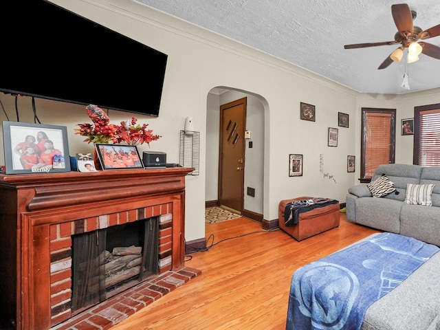 living room featuring hardwood / wood-style floors, ornamental molding, ceiling fan, a brick fireplace, and a textured ceiling