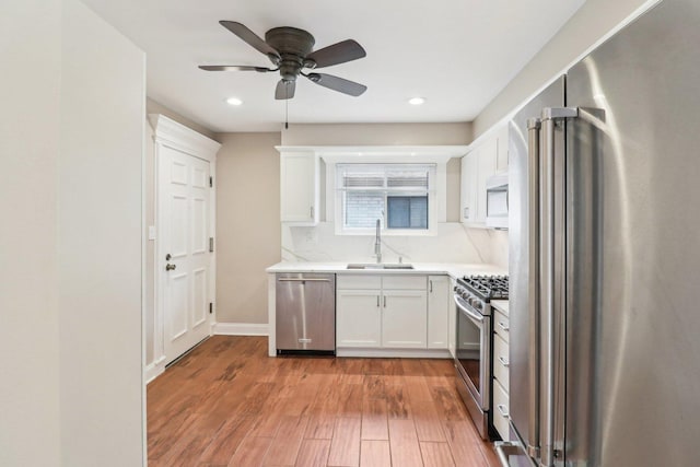 kitchen with sink, ceiling fan, appliances with stainless steel finishes, light hardwood / wood-style floors, and white cabinets