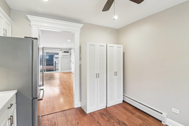 unfurnished bedroom featuring an AC wall unit, a baseboard radiator, stainless steel fridge, dark hardwood / wood-style flooring, and ceiling fan