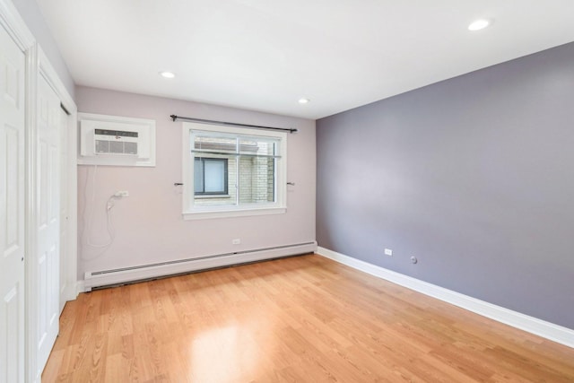 unfurnished room featuring light hardwood / wood-style floors, a wall unit AC, and a baseboard heating unit