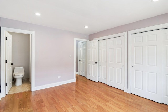 unfurnished bedroom featuring connected bathroom, light hardwood / wood-style flooring, and multiple closets