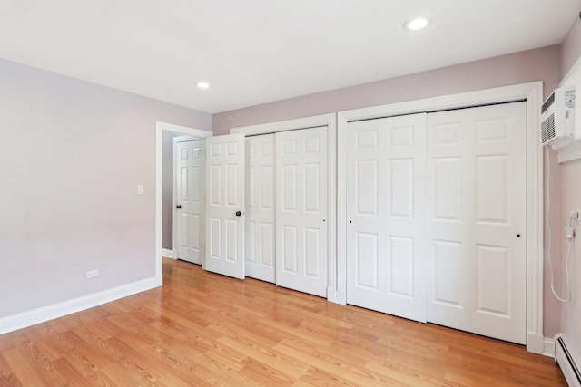 unfurnished bedroom with two closets, baseboard heating, and light hardwood / wood-style flooring