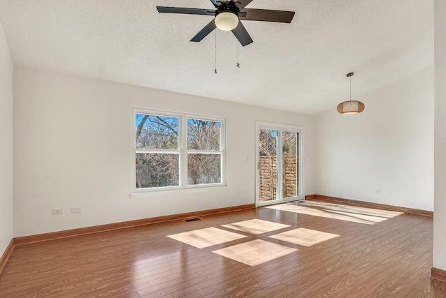 spare room with vaulted ceiling, a textured ceiling, baseboards, and hardwood / wood-style flooring