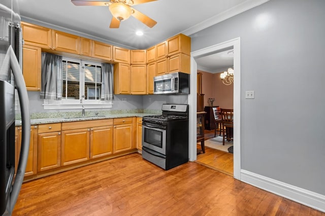 kitchen with sink, light stone counters, light hardwood / wood-style flooring, ornamental molding, and appliances with stainless steel finishes