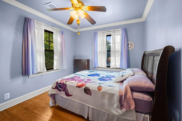 bedroom with crown molding, ceiling fan, wood-type flooring, and multiple windows