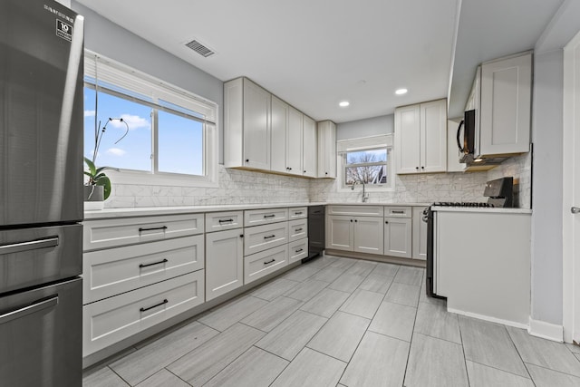 kitchen featuring sink, stainless steel fridge, white cabinets, stove, and backsplash