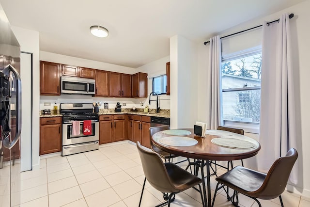 kitchen featuring brown cabinets, stainless steel appliances, light tile patterned flooring, a sink, and light stone countertops