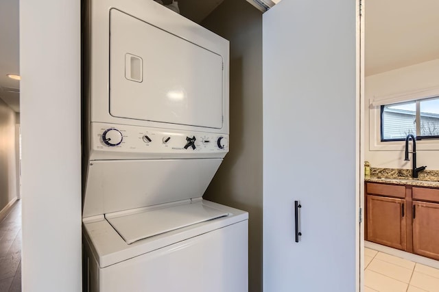 washroom featuring light tile patterned floors, laundry area, a sink, and stacked washer and clothes dryer