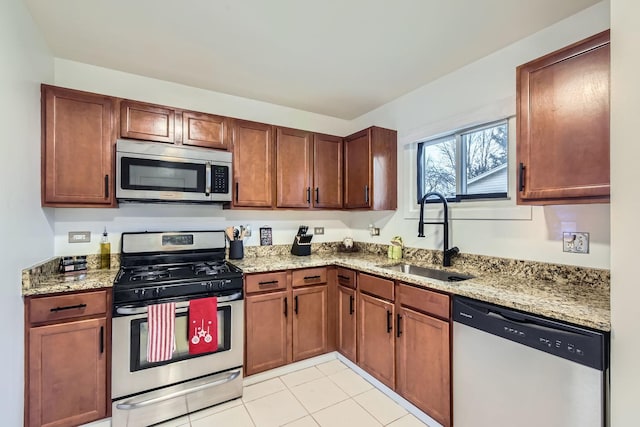 kitchen featuring light tile patterned floors, stainless steel appliances, a sink, and light stone countertops