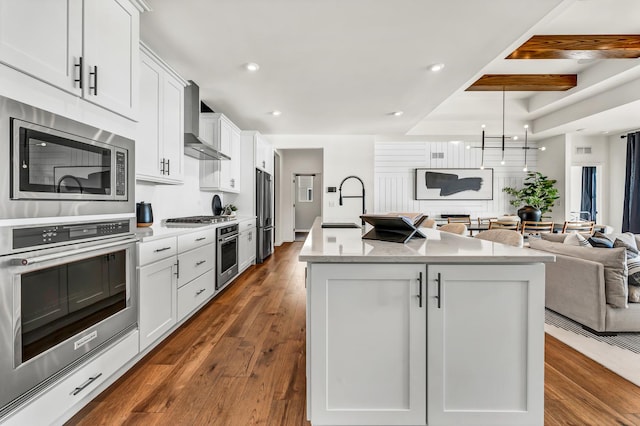 kitchen featuring white cabinetry, a kitchen island with sink, stainless steel appliances, and wall chimney exhaust hood