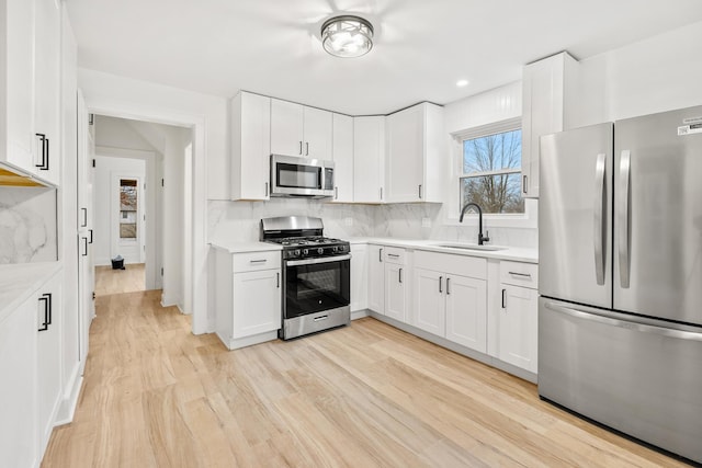 kitchen featuring appliances with stainless steel finishes, sink, white cabinets, backsplash, and light hardwood / wood-style floors