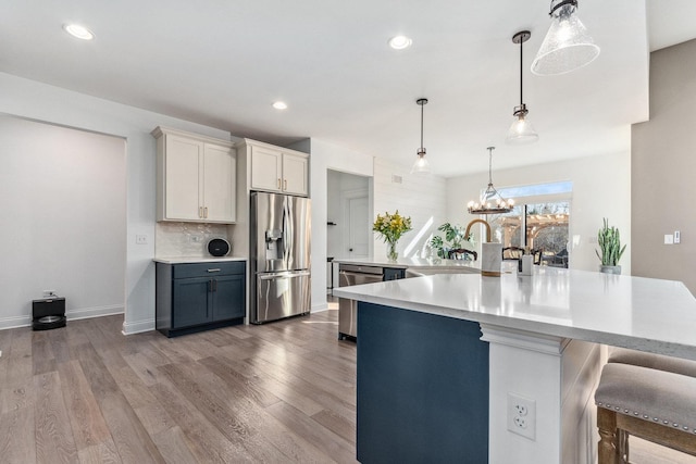 kitchen featuring pendant lighting, a breakfast bar, appliances with stainless steel finishes, white cabinetry, and hardwood / wood-style floors