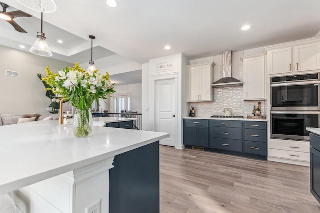 kitchen featuring wall chimney exhaust hood, decorative light fixtures, stainless steel appliances, decorative backsplash, and white cabinets