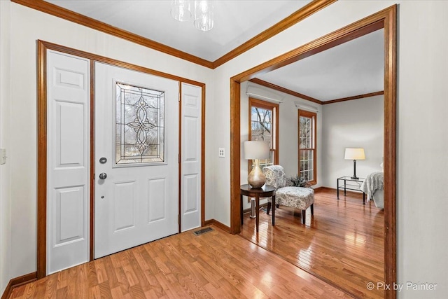 entryway with an inviting chandelier, ornamental molding, and light wood-type flooring