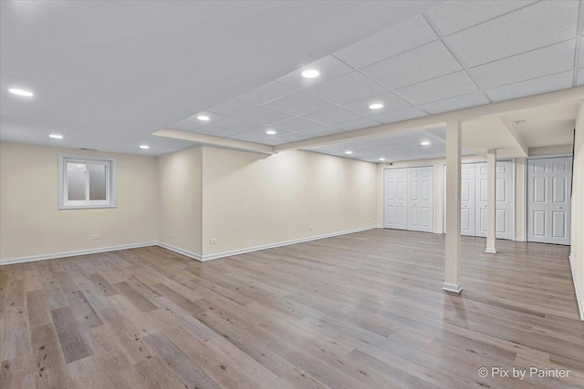 basement with light hardwood / wood-style flooring and a paneled ceiling