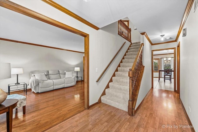 staircase with hardwood / wood-style flooring, crown molding, and a chandelier