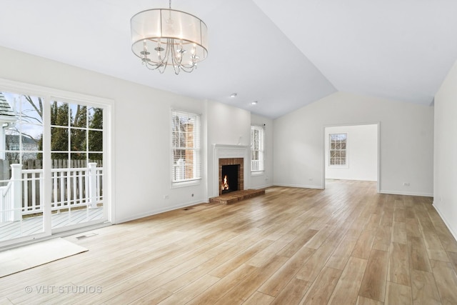 unfurnished living room featuring a notable chandelier, lofted ceiling, a fireplace, and light hardwood / wood-style floors