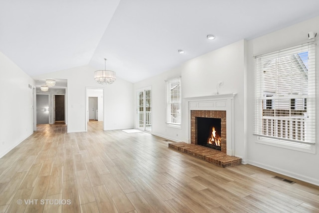 unfurnished living room with vaulted ceiling, an inviting chandelier, light hardwood / wood-style floors, and a brick fireplace