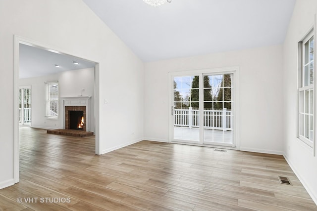 spare room featuring lofted ceiling, a brick fireplace, and light hardwood / wood-style floors