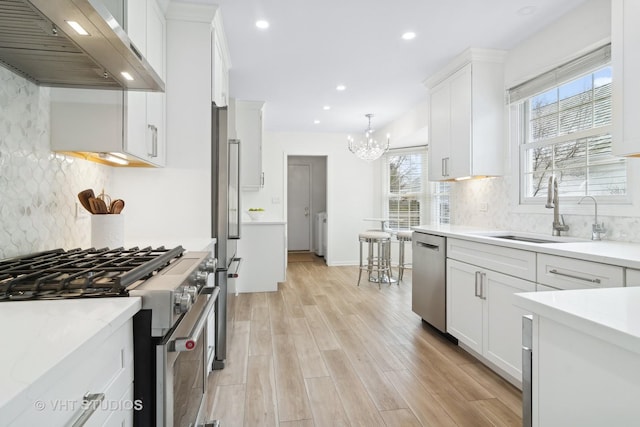 kitchen with sink, high end appliances, pendant lighting, range hood, and white cabinets