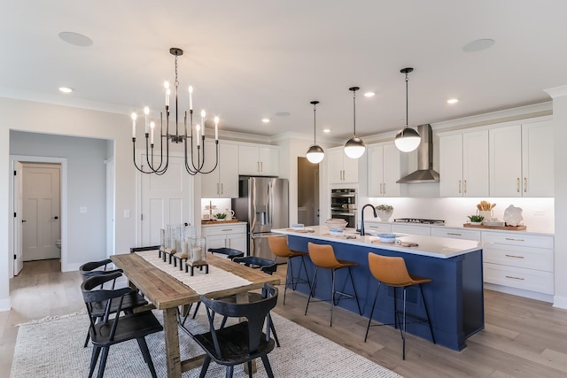 kitchen featuring wall chimney range hood, an island with sink, pendant lighting, stainless steel appliances, and white cabinets