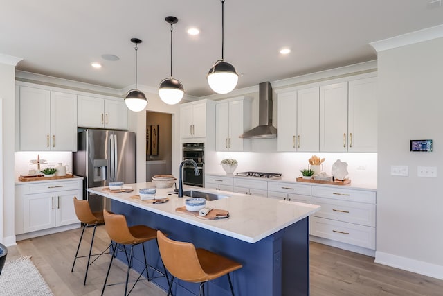 kitchen with wall chimney exhaust hood, sink, decorative light fixtures, stainless steel fridge, and an island with sink