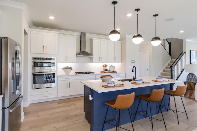 kitchen featuring wall chimney range hood, sink, appliances with stainless steel finishes, an island with sink, and white cabinets