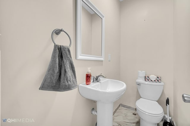 half bathroom featuring marble finish floor, a sink, toilet, and baseboards