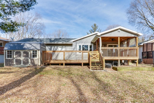 rear view of property featuring a wooden deck, ceiling fan, an outdoor structure, and a lawn