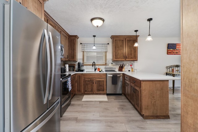 kitchen with sink, light hardwood / wood-style flooring, appliances with stainless steel finishes, decorative light fixtures, and kitchen peninsula