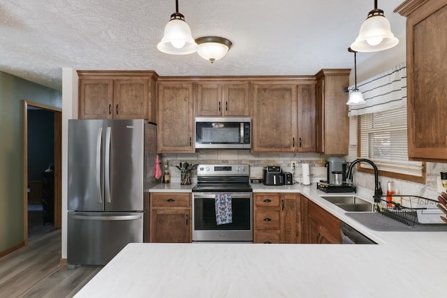 kitchen with sink, tasteful backsplash, wood-type flooring, appliances with stainless steel finishes, and pendant lighting