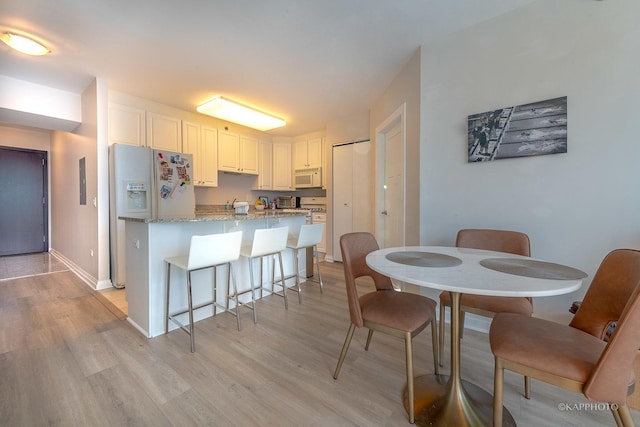 kitchen with white appliances, white cabinetry, a kitchen breakfast bar, light stone countertops, and light wood-type flooring