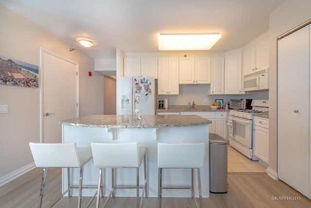 kitchen with white appliances, light stone countertops, a kitchen island with sink, and white cabinets