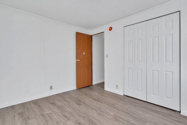 unfurnished bedroom featuring crown molding, a closet, light hardwood / wood-style flooring, and a textured ceiling