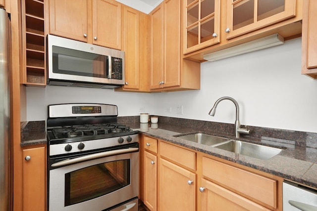 kitchen featuring dark stone counters, glass insert cabinets, appliances with stainless steel finishes, light brown cabinetry, and a sink