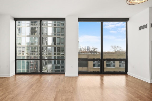 spare room with a wall of windows, visible vents, baseboards, and wood finished floors