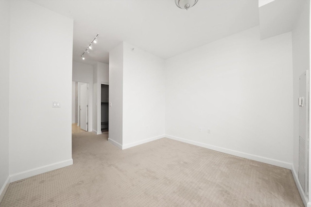 empty room with rail lighting, baseboards, and light colored carpet