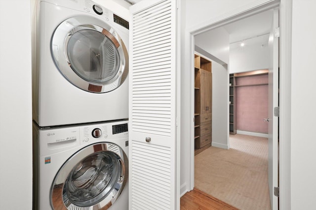 clothes washing area with carpet floors, stacked washer / dryer, laundry area, and baseboards