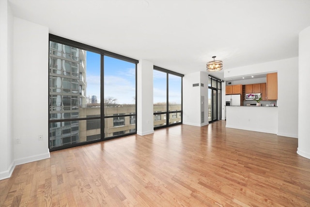 unfurnished living room with baseboards, a wall of windows, and light wood-style floors