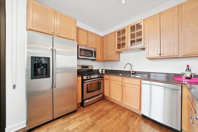 kitchen with light wood-style flooring, glass insert cabinets, stainless steel appliances, light brown cabinetry, and a sink