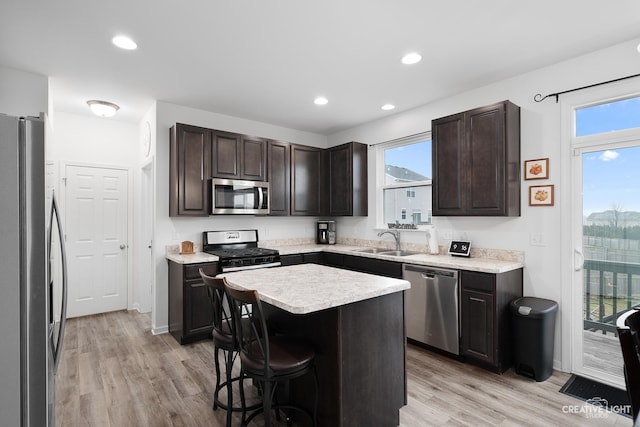 kitchen with sink, a breakfast bar area, appliances with stainless steel finishes, dark brown cabinets, and a kitchen island