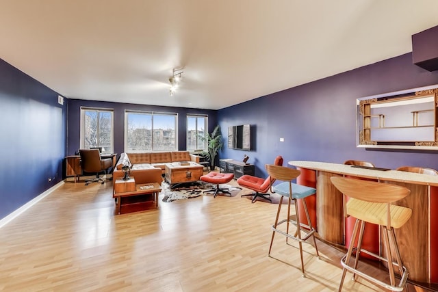 living room with bar area, baseboards, and light wood finished floors