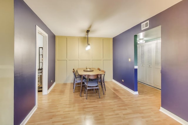 dining area featuring light wood-style flooring, a decorative wall, visible vents, and baseboards