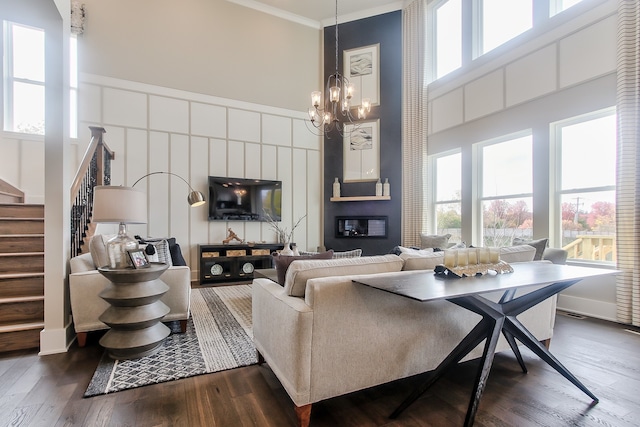 living room featuring dark wood-type flooring, ornamental molding, a chandelier, and a high ceiling